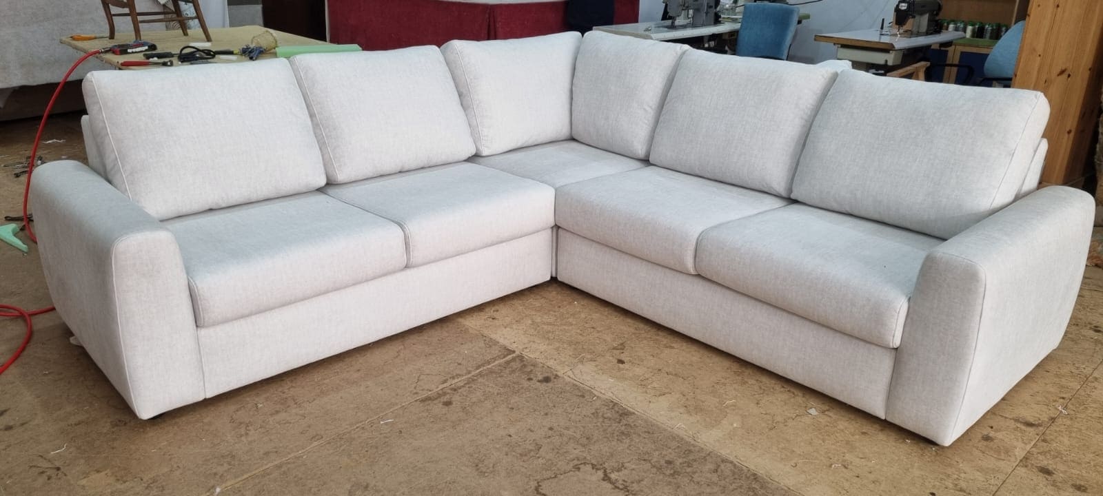 Sofá esquinero con brazos anchos y respaldo acolchado tapizado en tono neutro. Tapicero a domicilio